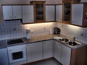 Una cucina con mobili bianchi, un fornello, una macchina da caffè e un lavello.