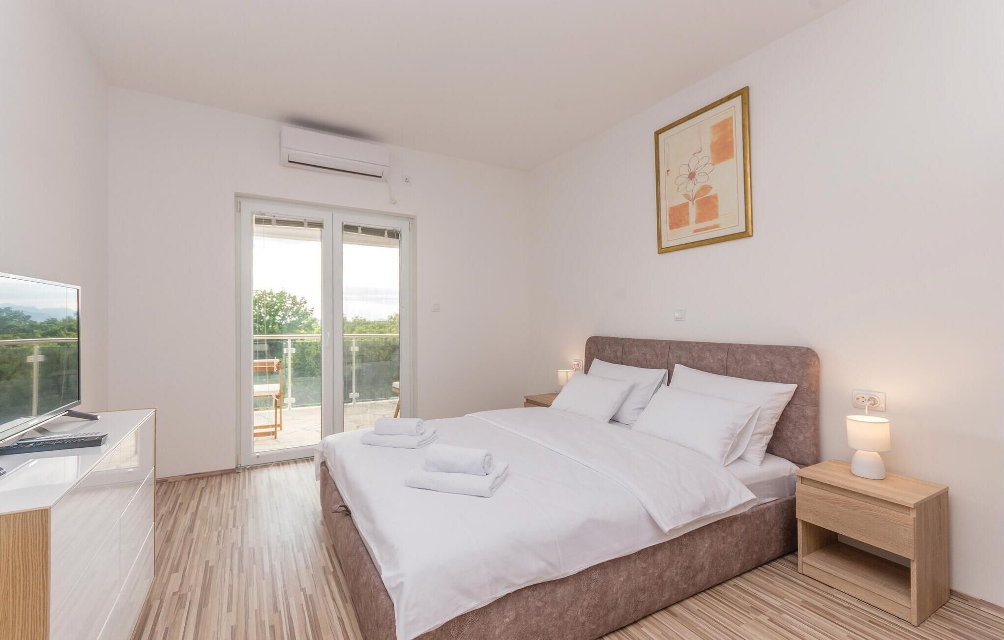 A bedroom with a bed, a nightstand, a desk, and a window with a view.