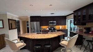 A modern kitchen with dark cabinetry, a granite countertop, and a central island with bar stools. - Island Living, Within Walking Distance To Beach Restaraunts Shops Parks Marina (Vero Beach)