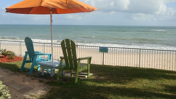 A beachside seating area with a large orange umbrella, two chairs, and a table. - Island Living, Within Walking Distance To Beach Restaraunts Shops Parks Marina (Vero Beach)