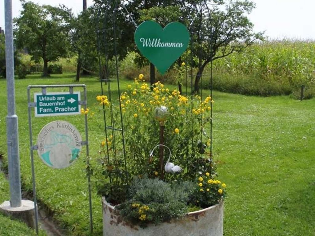 A garden with a heart-shaped sign saying 'Willkommen' and a directional sign for 'Uraub am Bauernhof Fam. Pracher'.
