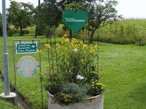 Un giardino con un cartello a forma di cuore che dice 'Willkommen' e un segnale direzionale per 'Urlaub am Bauernhof Fam. Pracher'.