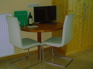 Un comedor con dos sillas, una mesa, un televisor y un mueble de almacenamiento.