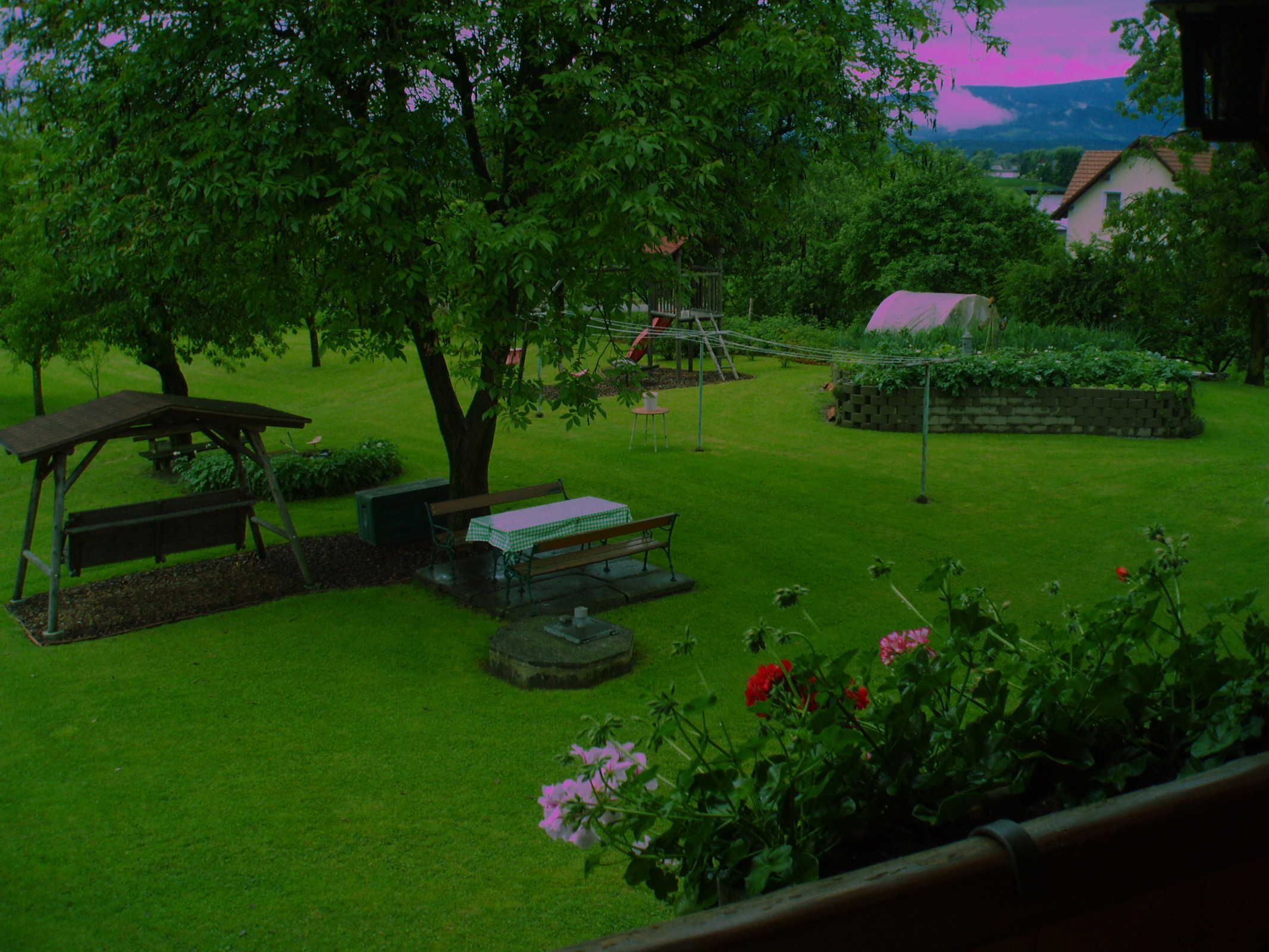 A garden with a picnic table, benches, a swing set, and a small building.