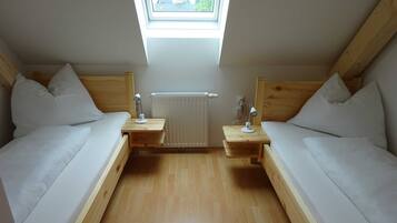 Une petite pièce bien éclairée, avec deux lits, des têtes de lit en bois et une lucarne.