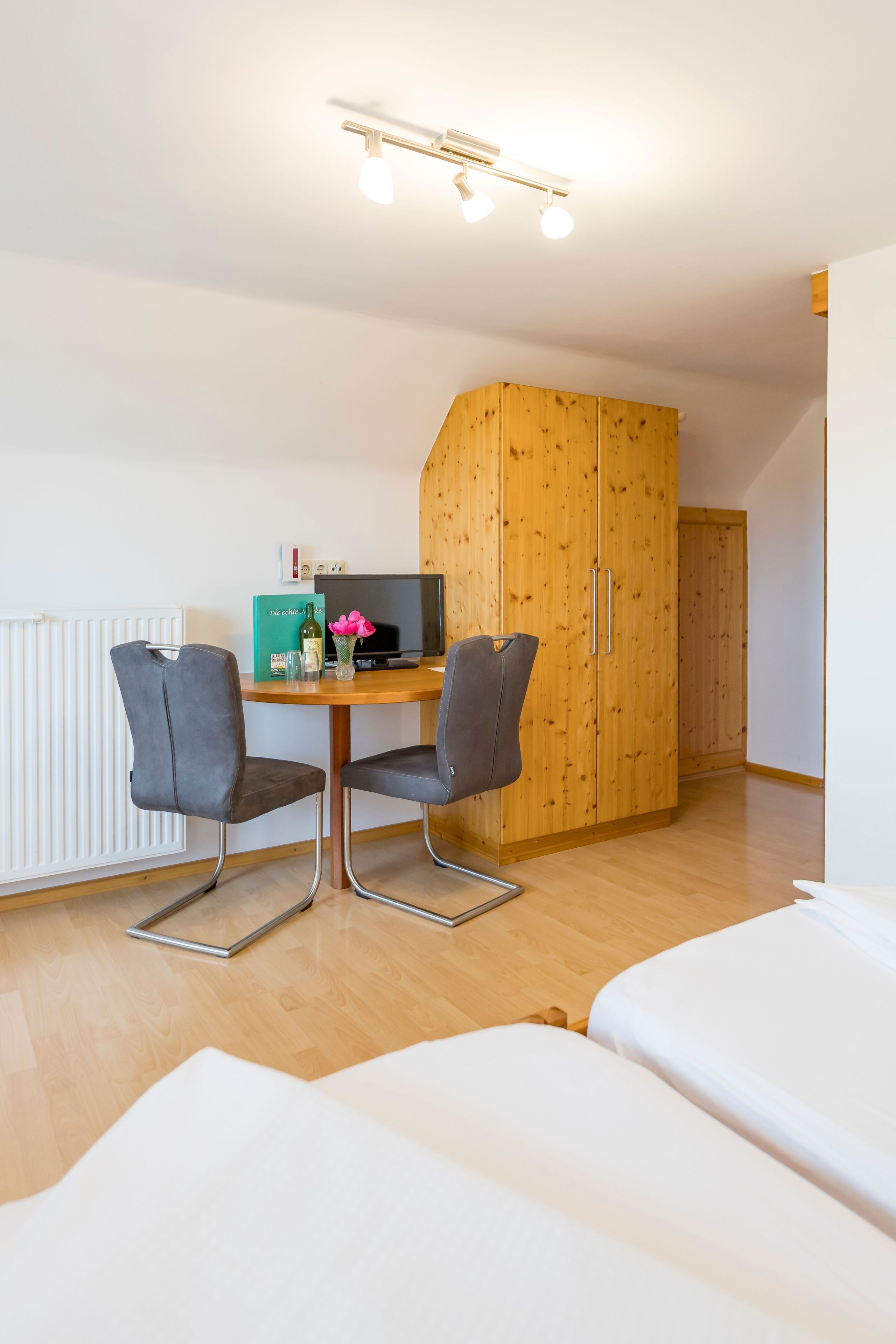 Una habitación con un armario de madera, un escritorio con dos sillas, una computadora y una cama.