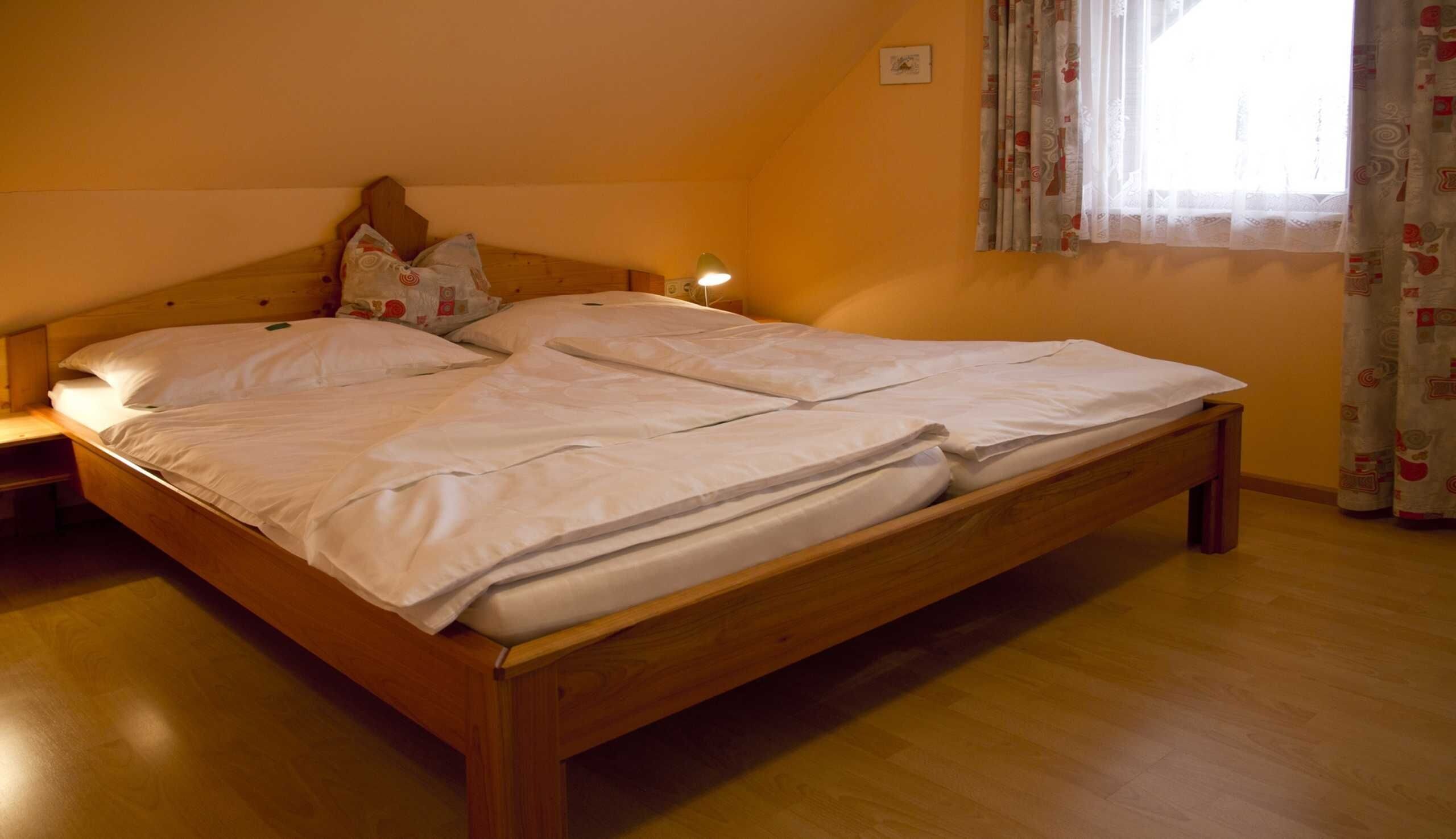 A single bed with a wooden frame, white bedding, and a nightstand with a lamp.