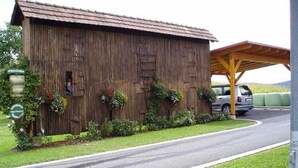 Un edificio de madera rústico con un porche cubierto, una carretera al frente y un coche estacionado cerca.