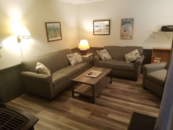 A living room with two sofas, a coffee table, and a lamp. There are framed pictures on the wall.