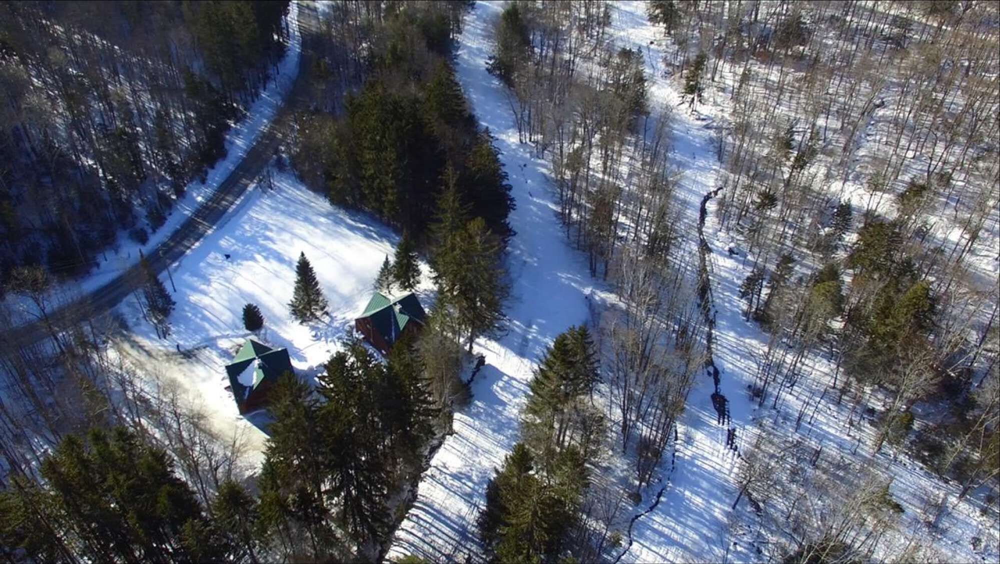An aerial view of a cabin surrounded by snow-covered ground and trees.