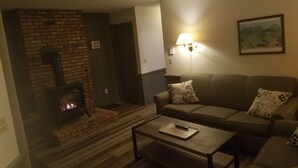 Un salon avec une cheminée en briques, un canapé, une table basse et une lampe fixée au mur.