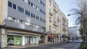 Ein mehrstöckiges Gebäude mit moderner Fassade, ein Geschäft im Erdgeschoss und eine Straße mit Autos und Fußgängern.