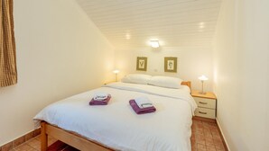 A bedroom with a bed, two bedside tables, a nightstand, a wall-mounted lamp, and two framed pictures on the wall. - Stunning home in Njivice with WiFi (Njivice)