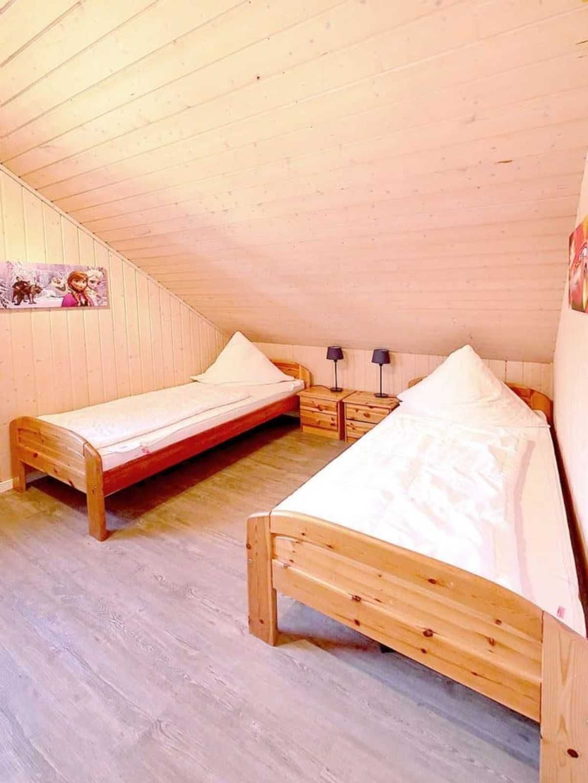 Un dormitorio acogedor en el ático, con dos camas de madera, una mesita de noche y una lámpara de pared.
