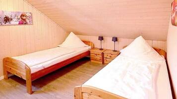 Un dormitorio acogedor en el ático, con dos camas de madera, una mesita de noche y una lámpara de pared.