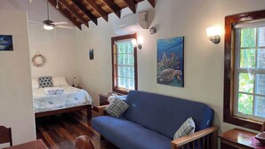 Una habitación acogedora con cama, un sofá azul, suelo de madera, ventilador de techo y ventana con un cuadro de una tortuga.
