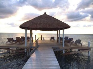 A wooden pier leading to a thatched-roof gazebo with lounge chairs. - Studio w/Pool, AC, Dock Access, Free Paddle boards (Caye Caulker)