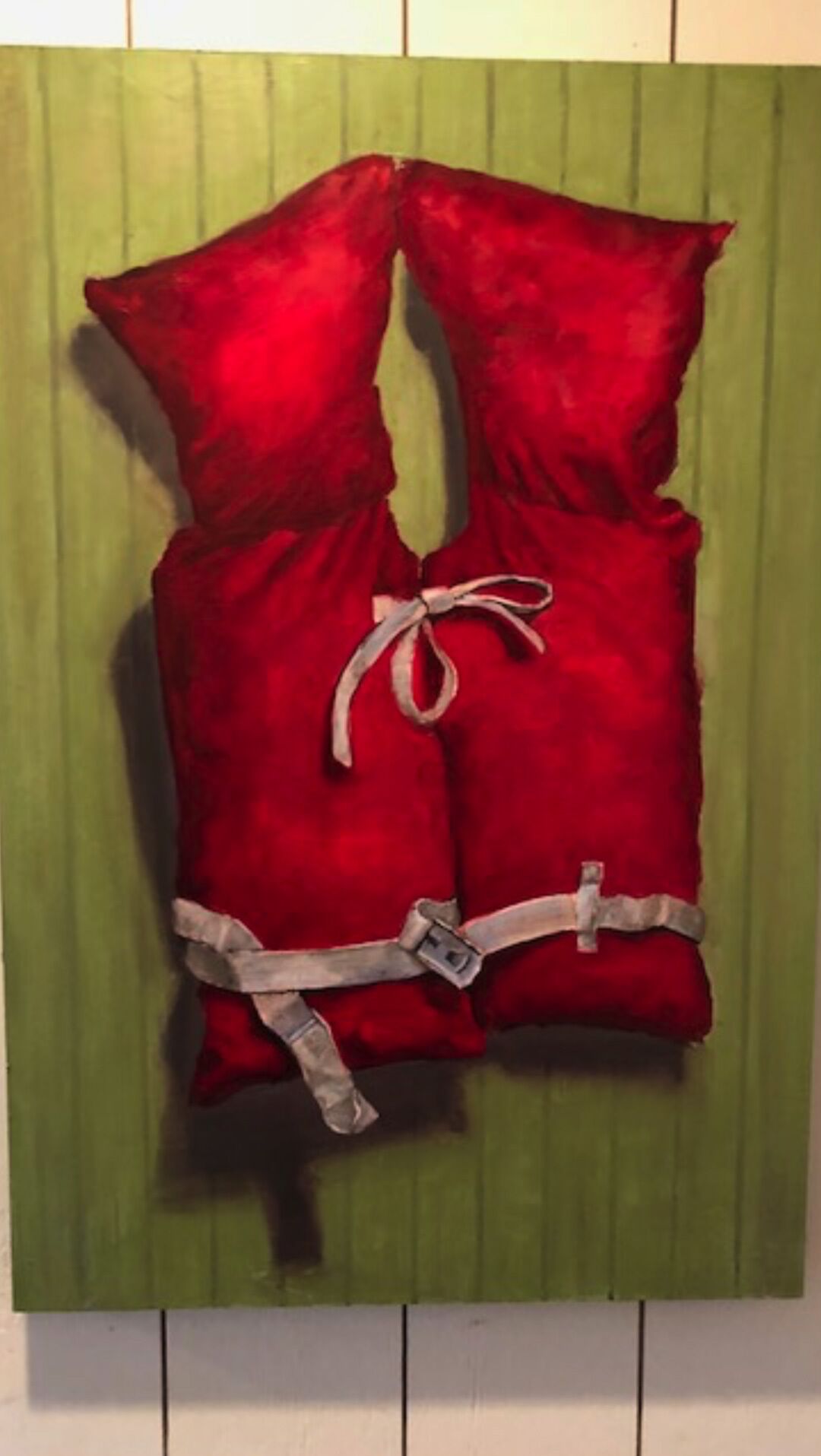 A pair of red pillows with a white ribbon and buckle on a green wall.
