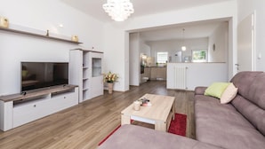 Een moderne woonkamer met een flatscreen-televisie, een bank, een salontafel en een keuken op de achtergrond.