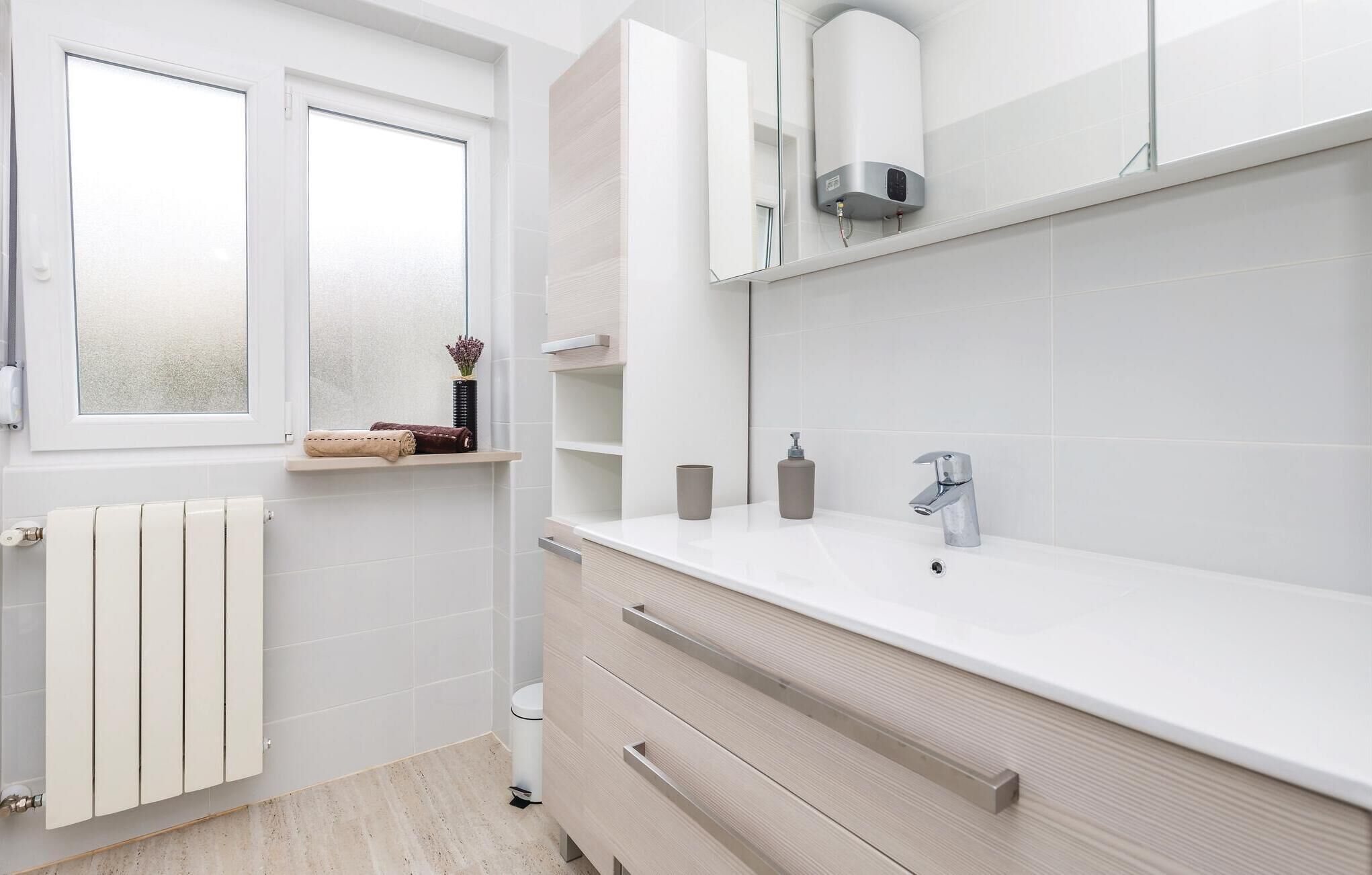 Een moderne badkamer met een wit badkamermeubel, toilet, radiator en een raam.