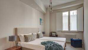 Un dormitorio con dos camas, una mesita de noche, una lámpara, una silla, un radiador y una ventana.