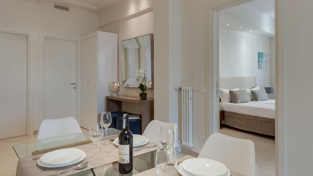 Una habitación de hotel moderna con zona de comedor, cama y un espejo grande.