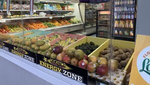 Um supermercado com diversas frutas e legumes expostos, incluindo uma seção identificada como 'Energy Zone' com bebidas energéticas.