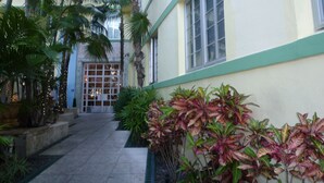 Um edifício com fachada clara e detalhes verdes, apresentando uma grande janela e uma porta com painéis de vidro.