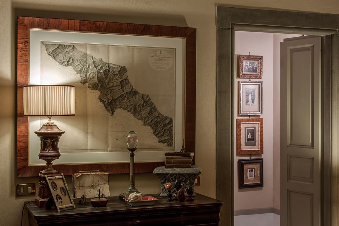A framed map on a wall, a lamp, a small table with decorative items, and framed pictures on the wall.
