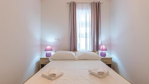 A single bed with two pillows and two folded towels, flanked by nightstands with lamps, in a room with a window and curtains. - Gorgeous home in Sikici (Sikici)
