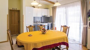 A dining area with a yellow table, chairs, and a flower centerpiece. There is a kitchen in the background with cabinets and a stove. - Gorgeous home in Sikici (Sikici)
