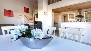 Une cuisine moderne avec des meubles blancs, une hotte en acier inoxydable et un coin repas comprenant une table et des chaises blanches.
