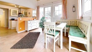 Une pièce chaleureuse comprenant une cuisine, un coin repas et un espace détente avec un banc rembourré de couleur verte.