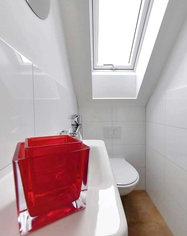 A modern bathroom with a white sink, a red glass soap dish, and a skylight above the toilet.