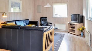 A cozy living room with a black leather sofa, a wooden chair, a television on a wooden stand, and a window with curtains. - Amazing home in Give with sauna (Give)