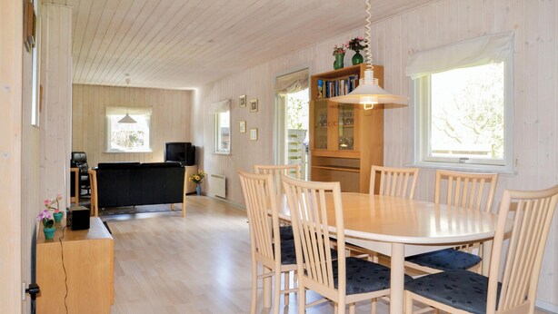 A dining area with a wooden table and chairs, a bookshelf, and a television in the background. - Amazing home in Give with sauna (Give)