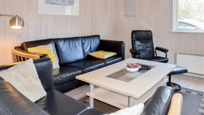A modern living room with a black leather sofa, a matching armchair, a glass-top coffee table, and a white side table. - Amazing home in Give with sauna (Give)