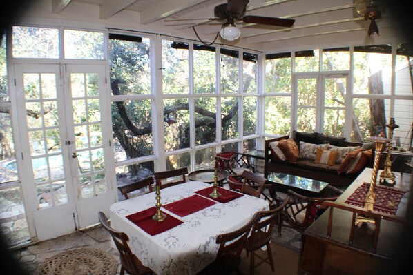 A sunlit room with a dining table set for four, a sofa, and a ceiling fan.