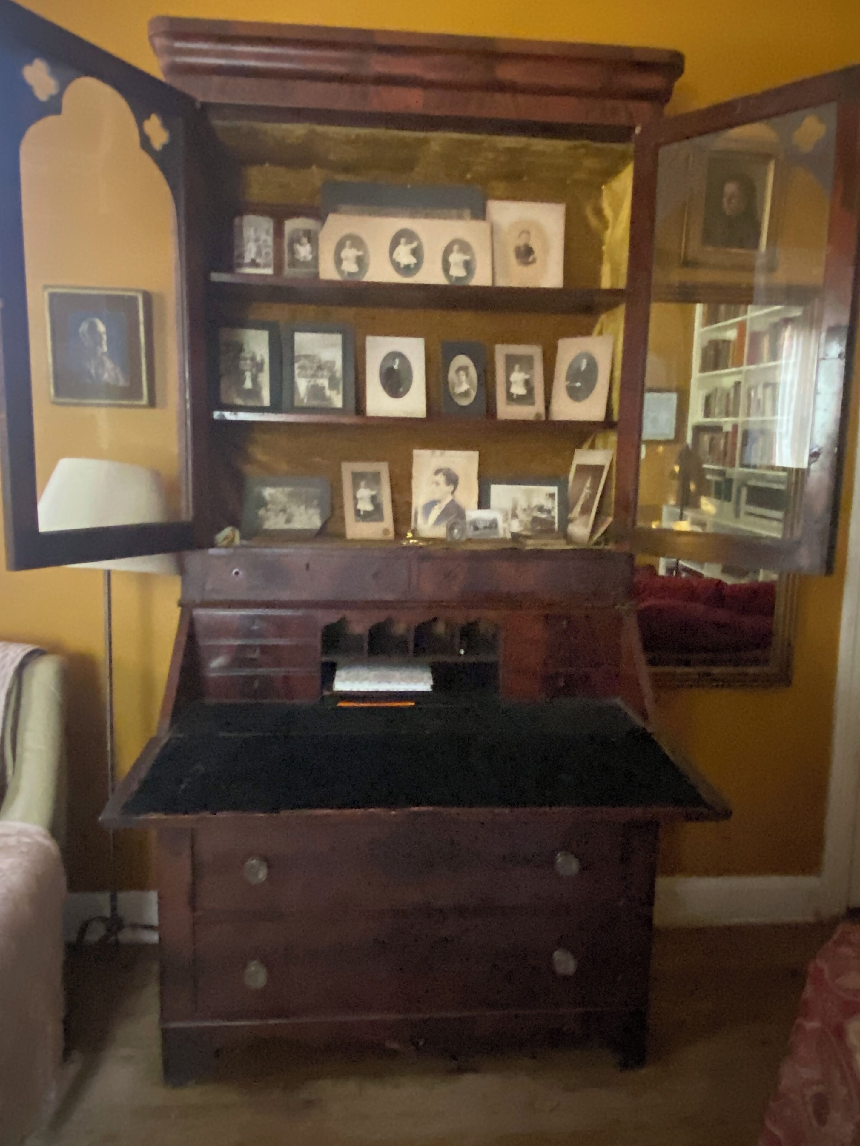 A room with a wooden desk, a mirror, and a wall-mounted photo display.