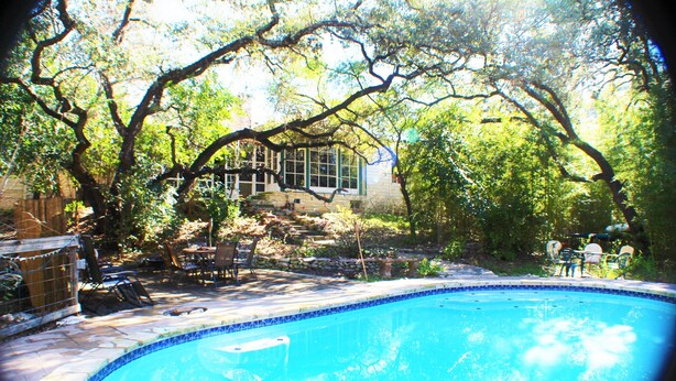 Piscina rodeada de árboles y un patio con mobiliario exterior.
