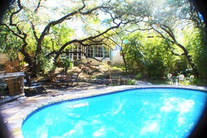 A swimming pool surrounded by trees and a patio area with outdoor furniture.