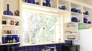 Una cocina con ventana, armarios blancos, azulejos azules y diversos electrodomésticos.