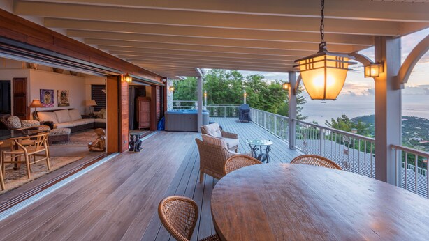 Een houten terras met buitenmeubilair, uitzicht op de oceaan en een hanglamp.