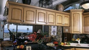 Een keuken met houten kastjes, een zwart aanrecht en een fornuis. Er staan fruit en bloemen op het aanrecht.