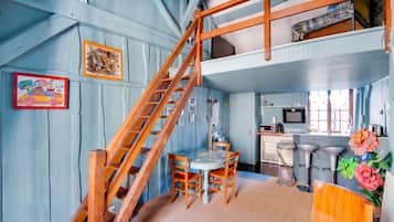 Une pièce avec un escalier en bois, une table à manger avec des chaises, un coin cuisine et un espace en mezzanine.