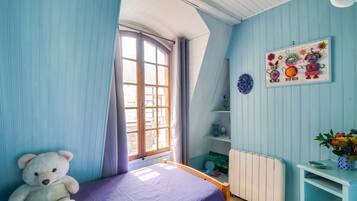 A room with a bed, a teddy bear, a radiator, a shelf with decorative items, and a window with curtains.