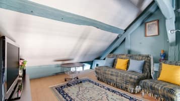 Um quarto de sótão acolhedor, com teto alto, um conjunto de sofás, uma mesinha redonda e uma televisão.