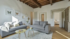 Una sala de estar con un sofá gris, dos mesitas, techo de madera y un armario.