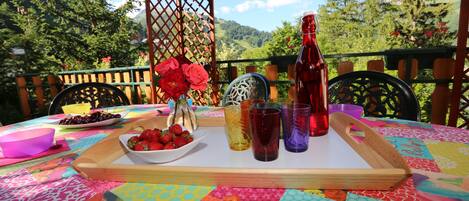 Una mesa dispuesta con una bandeja, cuencos de fresas y uvas, una botella y vasos, con una vista panorámica de montañas al fondo.