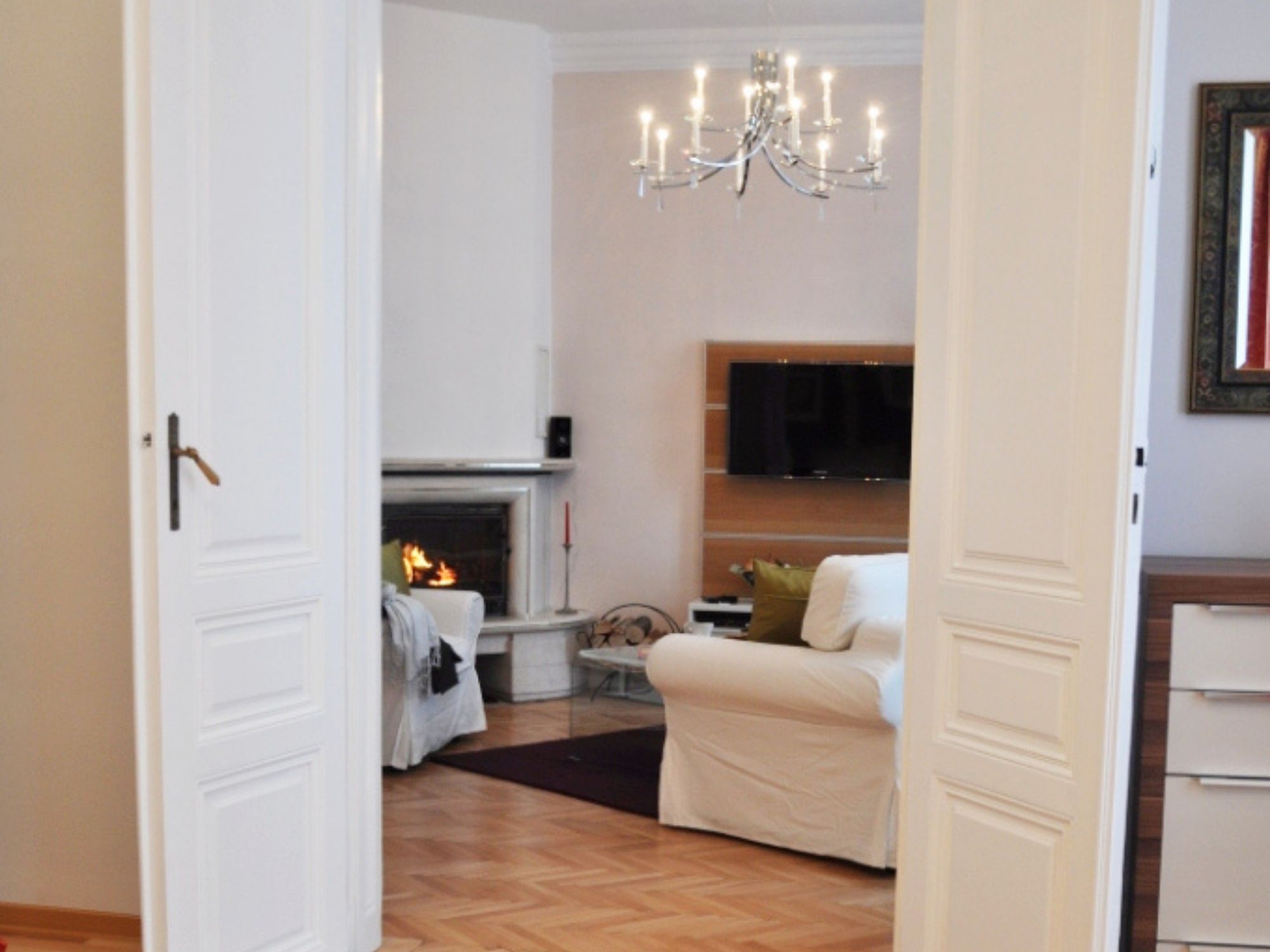 Ein Wohnzimmer mit Kamin, einem weißen Sofa, einem Fernseher und einer Chandelüster.